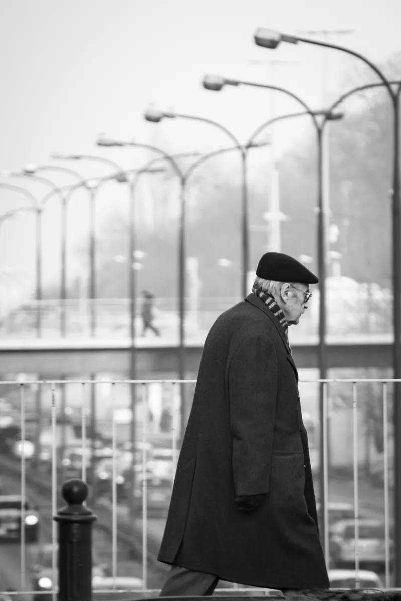 Man in a dark coat walking beneath a row of streetlights